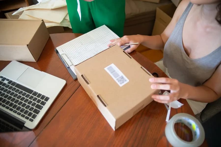 Dizüstü bilgisayarın yanında sipariş kolisi paketleyen iki kişi